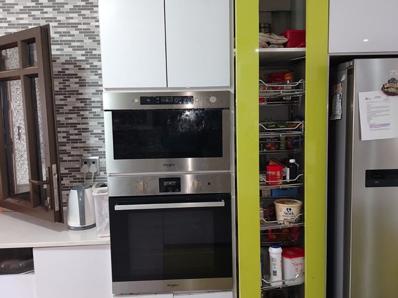 Modern kitchen featuring white cabinetry, a built-in oven and microwave, and a convenient pull-out pantry with a vibrant lime green accent door.