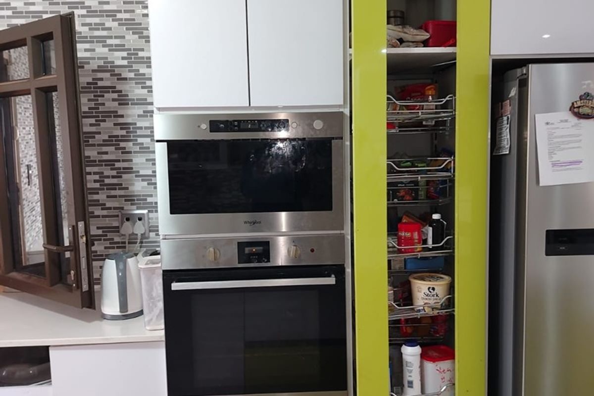 Modern kitchen featuring white cabinetry, a built-in oven and microwave, and a convenient pull-out pantry with a vibrant lime green accent door.