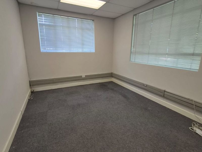 A vacant office space featuring a suspended ceiling, recessed lighting, venetian blinds, and surface-mounted electrical trunking along the walls.