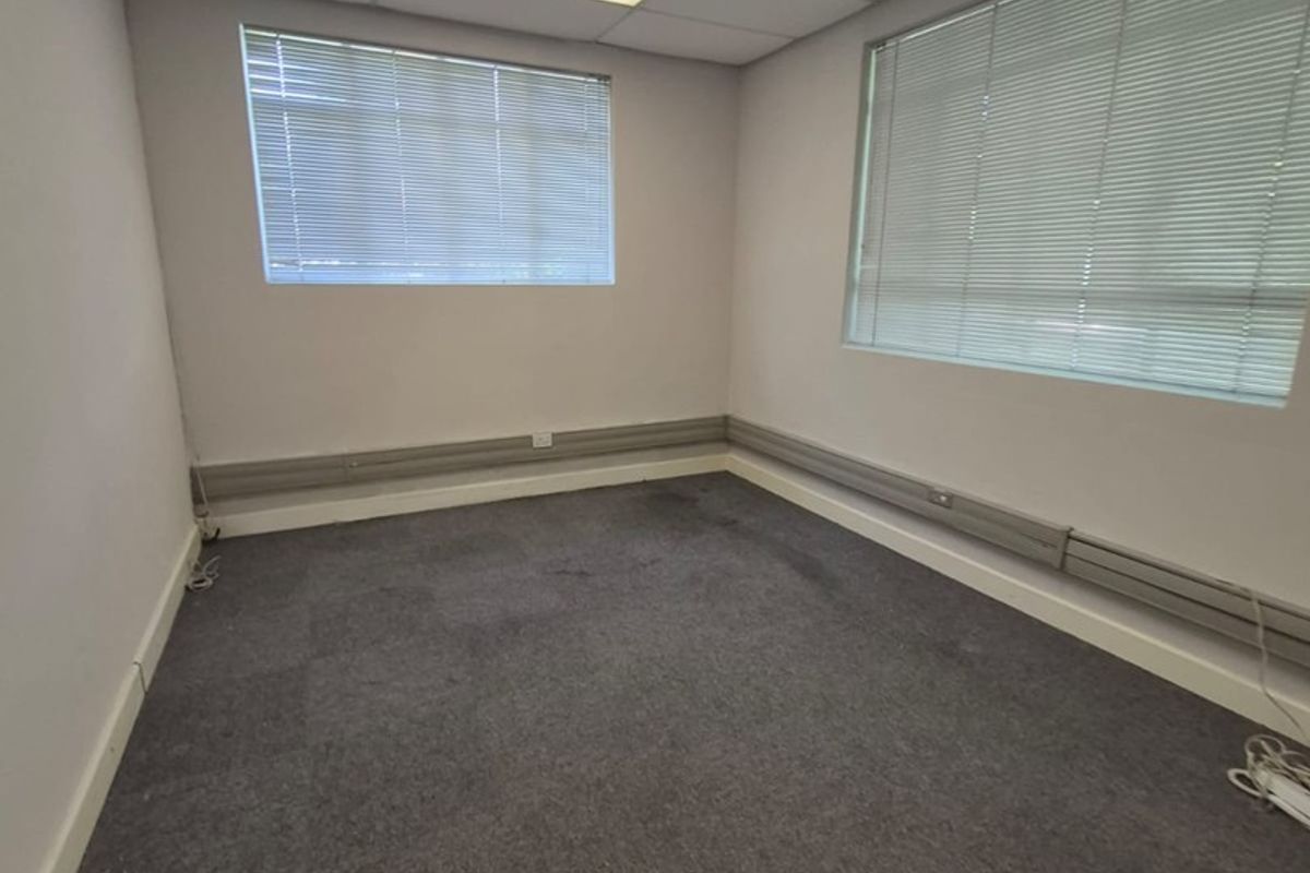 A vacant office space featuring a suspended ceiling, recessed lighting, venetian blinds, and surface-mounted electrical trunking along the walls.
