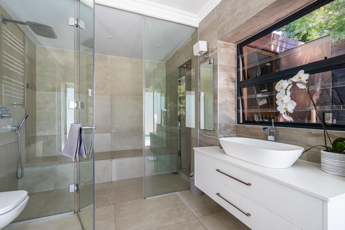 Modern bathroom featuring a spacious walk-in shower with a built-in bench, a sleek wall-mounted vanity with a vessel sink, and a heated towel rail.