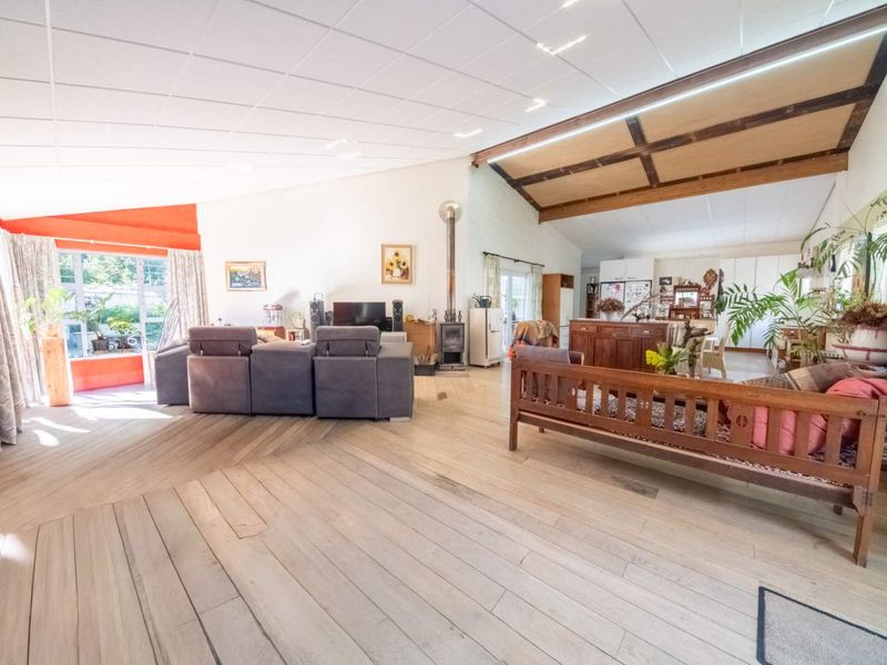 Spacious open-plan living area featuring timber flooring, exposed ceiling beams, and a wood-burning stove, offering a versatile layout with abundant natural light.