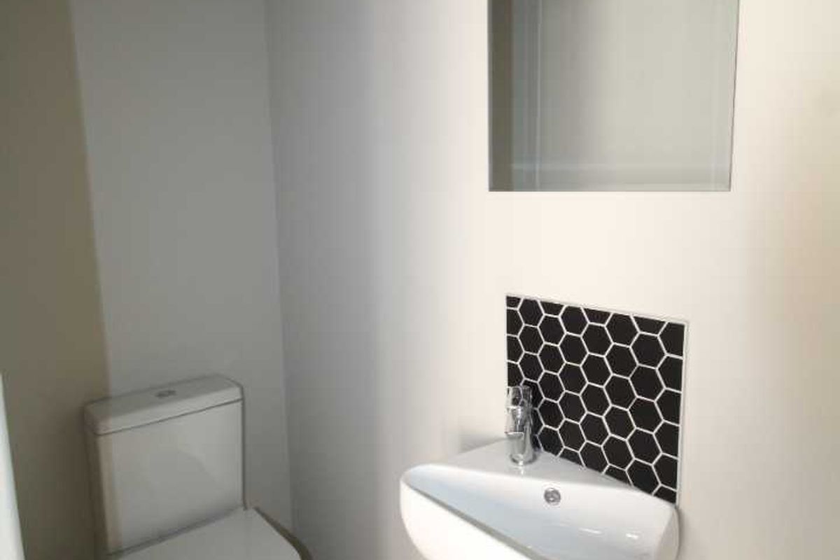 A compact guest cloakroom featuring a modern wall-mounted basin with a decorative hexagonal tile splashback and a standard white toilet.