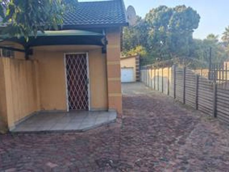 Front exterior view of the property featuring a paved driveway, covered porch entrance with security gate, and perimeter walling.