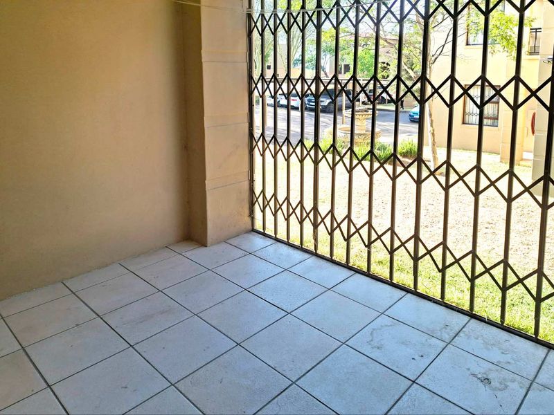 A covered patio area featuring tiled flooring and a secure metal gate, providing a functional outdoor space with views of the complex grounds.