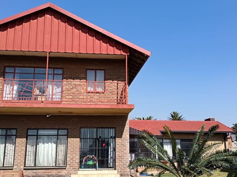 Rear view of a two-story brick house featuring a red metal roof, an upper-level balcony with metal railings, and security bars on windows and doors.