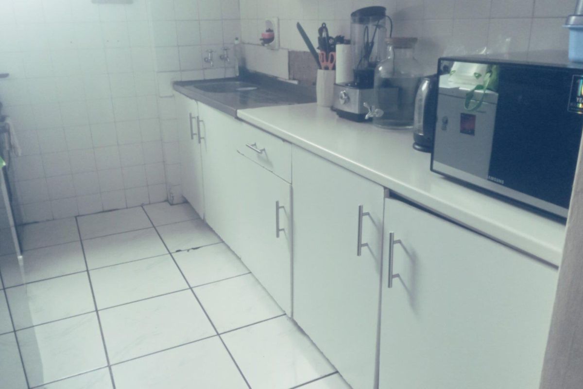 A compact kitchen featuring white cabinetry, tiled flooring, and wall-mounted tiling, providing a functional workspace with integrated sink and counter area.