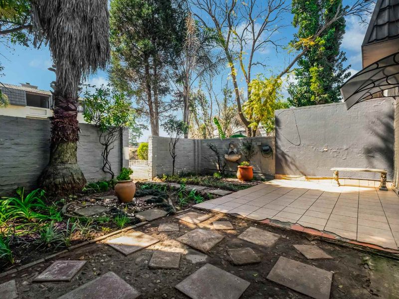 A private rear courtyard featuring a tiled patio area, stone paving, established garden beds, and a wall-mounted water feature.