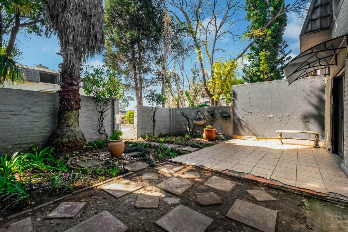 A private rear courtyard featuring a tiled patio area, stone paving, established garden beds, and a wall-mounted water feature.