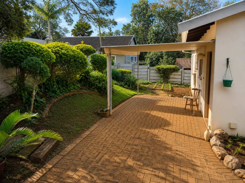 A well-maintained paved patio area with a covered veranda, overlooking a landscaped garden with established shrubs and a secure boundary wall.