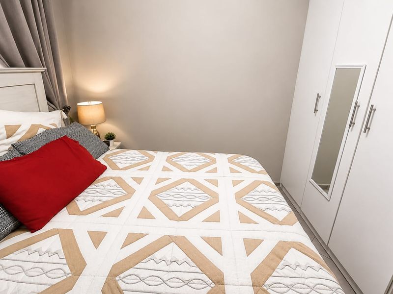 A well-maintained bedroom featuring a modern white built-in wardrobe with a central mirror panel and neutral wall finishes.