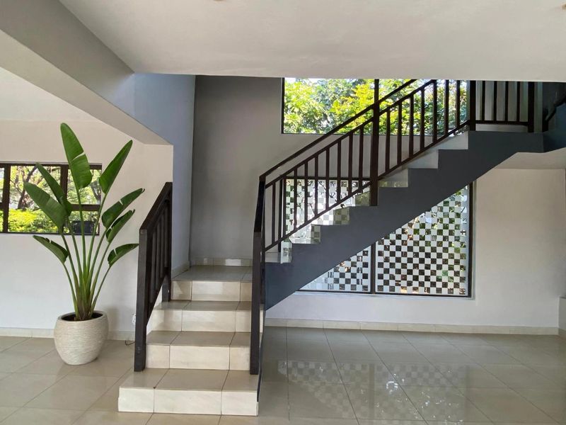 Spacious entrance hall featuring a modern staircase with timber balustrades, tiled flooring, and large windows with decorative privacy film.
