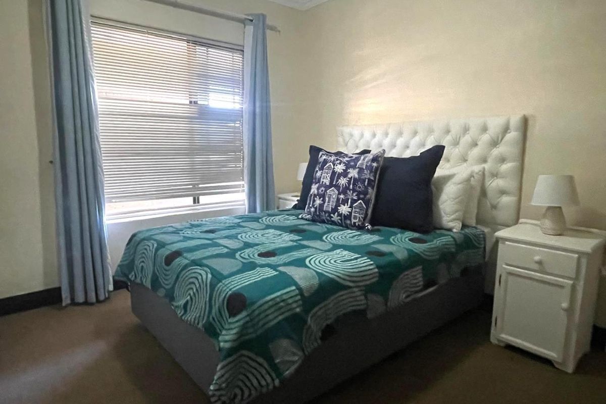 A cozy bedroom featuring carpeted flooring, neutral wall finishes, and a window fitted with venetian blinds and curtain rails.