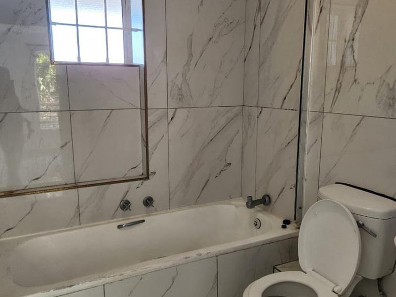 A bathroom featuring marble-look wall tiles, a built-in bathtub with a shower head, a glass screen, and a standard toilet.
