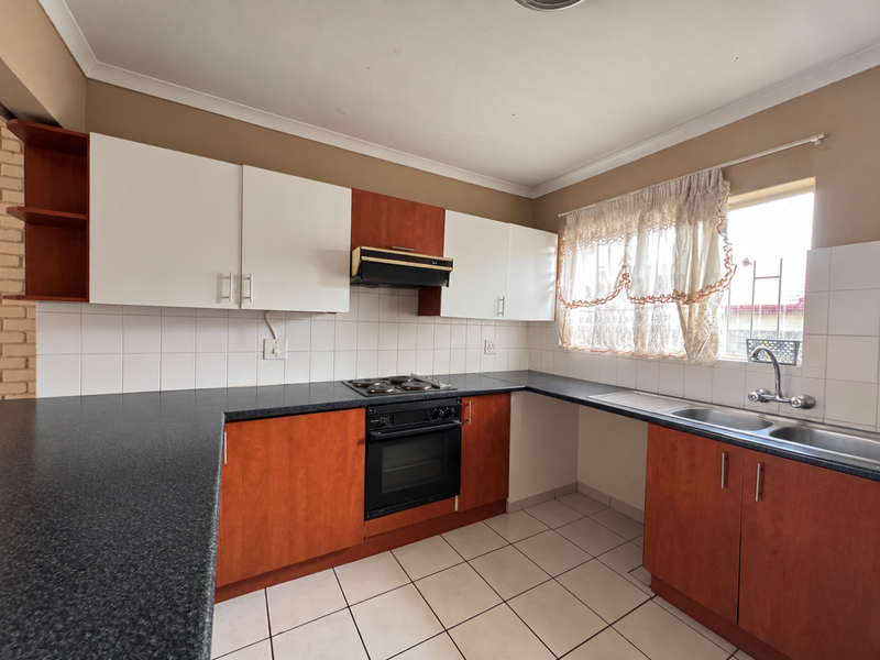 A functional kitchen featuring built-in cabinetry, a dark laminate countertop, an integrated oven and hob, and a double sink with tiled backsplash.