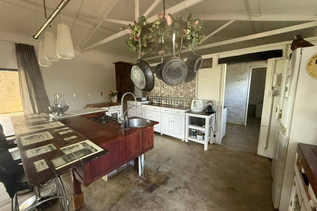 Rustic farm-style kitchen featuring a central island, built-in cabinetry, tiled backsplash, and exposed ceiling rafters with a concrete floor.