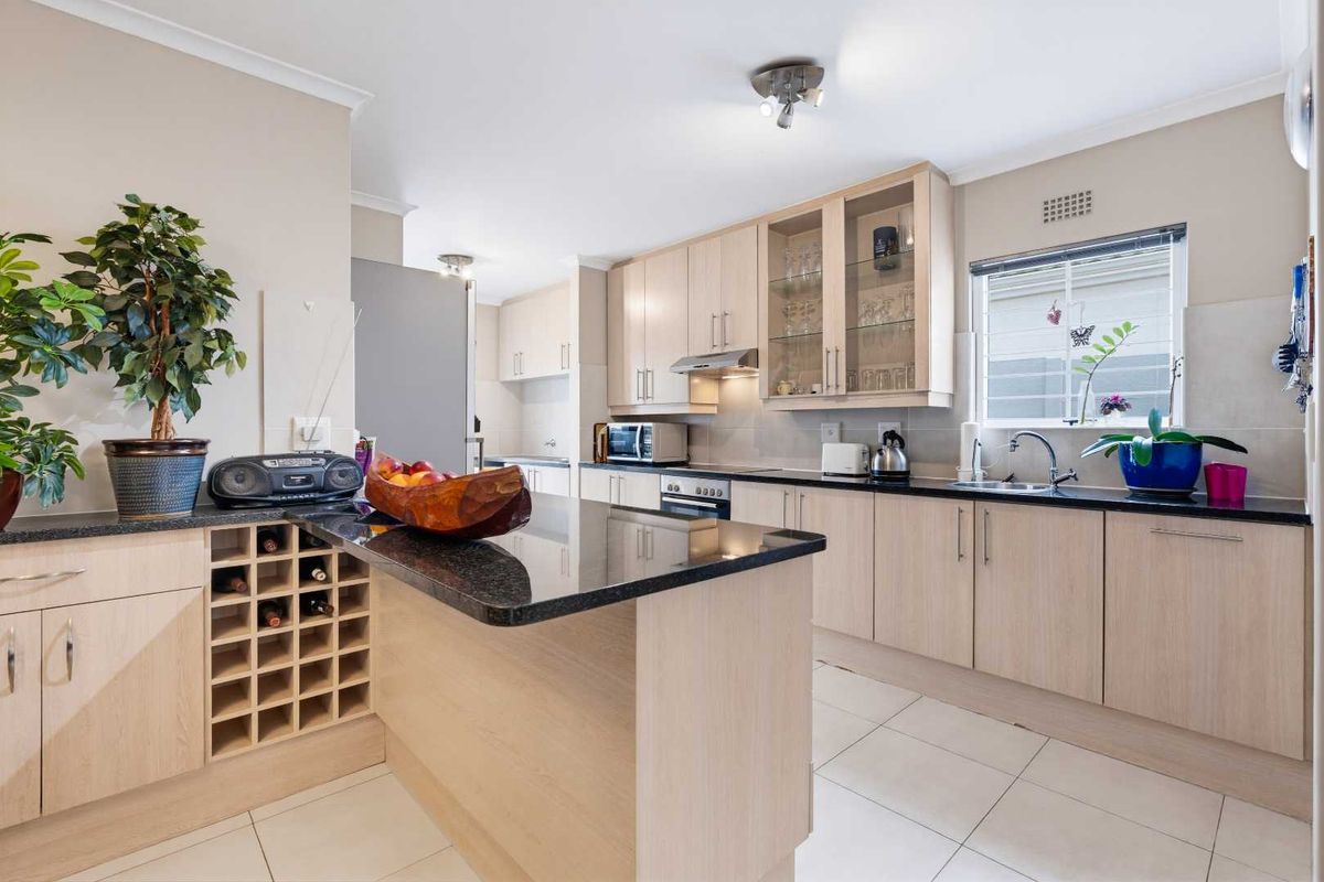 A well-maintained kitchen featuring light wood cabinetry, granite countertops, a built-in oven, extractor fan, and a dedicated wine rack.