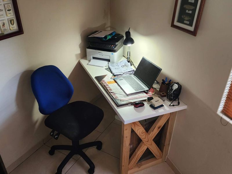 A compact home office corner featuring a built-in desk, tiled flooring, and venetian blinds, providing a functional workspace.