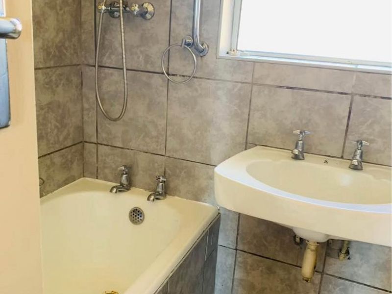 A functional bathroom featuring a bathtub with shower attachment, wall-mounted basin, and neutral tiled finishes throughout.
