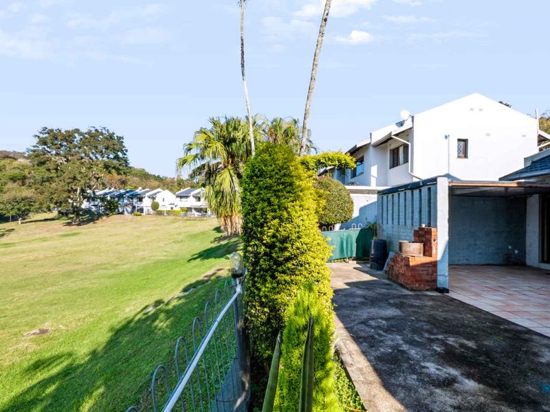 Rear exterior view of the townhouse featuring a paved patio area with a built-in brick braai, overlooking a spacious communal green lawn.