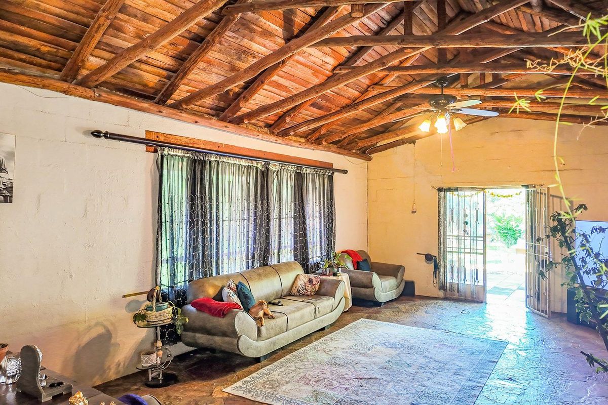 Spacious living room featuring a high vaulted timber-beamed ceiling, rustic stone flooring, and direct access to the outdoor area.