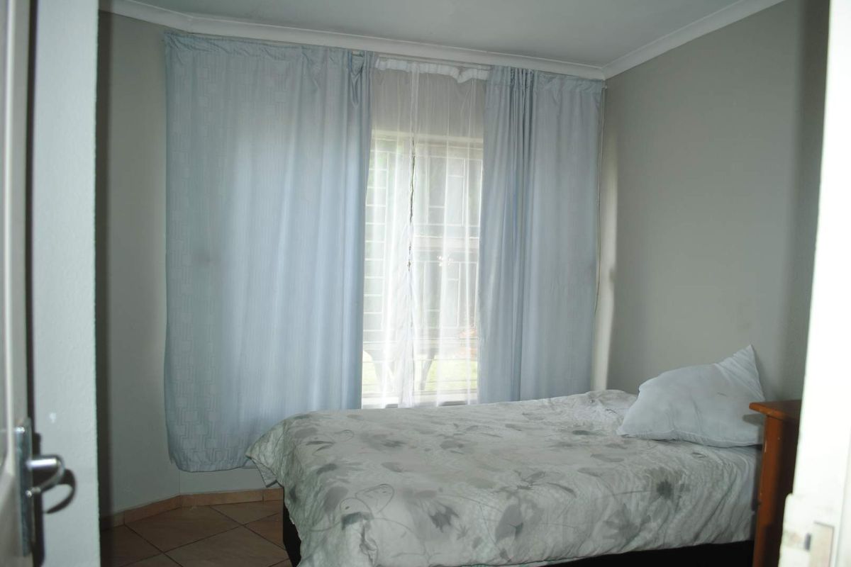 A standard bedroom featuring tiled flooring and a window with security bars, providing natural light and a functional living space.