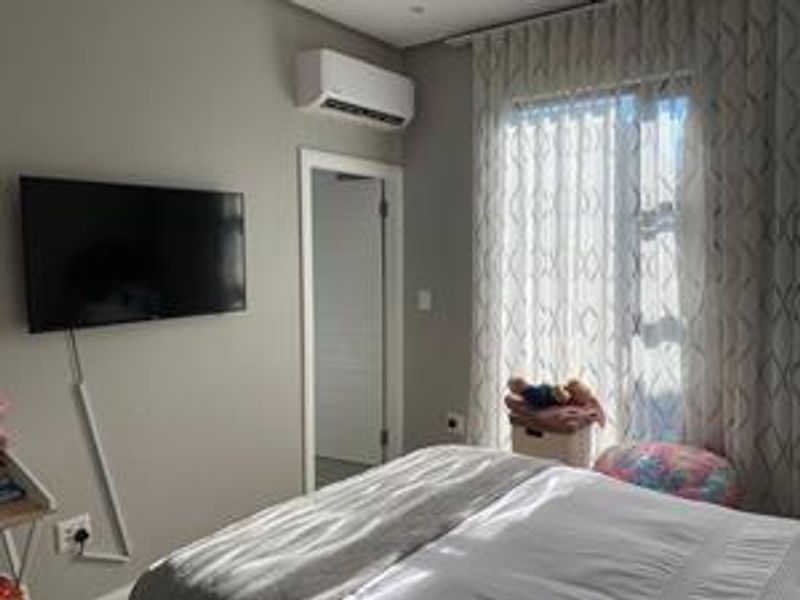 A well-maintained bedroom featuring a wall-mounted air conditioning unit, neutral wall finishes, and large windows with installed curtain tracks.