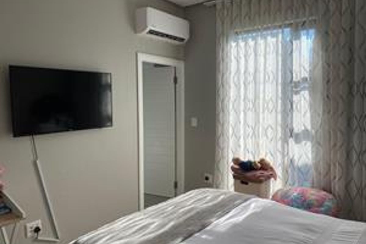 A well-maintained bedroom featuring a wall-mounted air conditioning unit, neutral wall finishes, and large windows with installed curtain tracks.