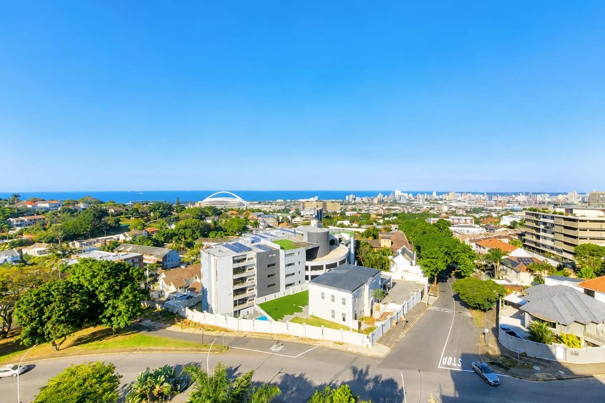 Aerial view of the penthouse property showing the building complex, surrounding neighbourhood, and distant coastal city skyline.