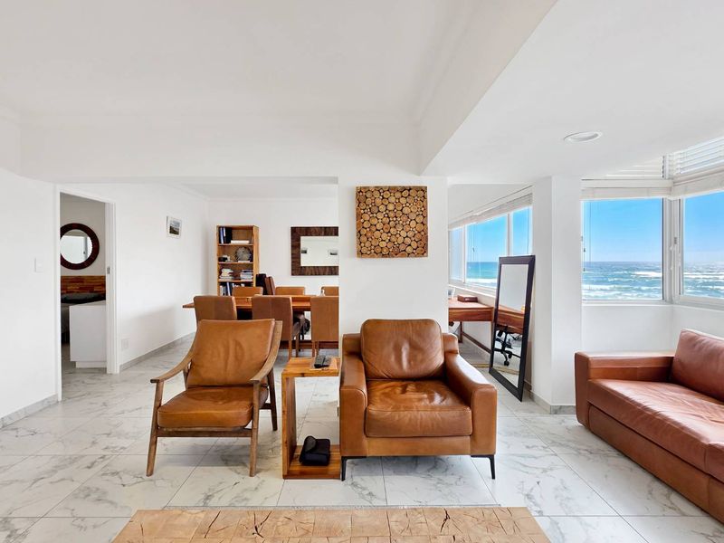 Spacious open-plan living and dining area featuring marble-look tiled flooring, recessed lighting, and expansive windows offering panoramic ocean views.