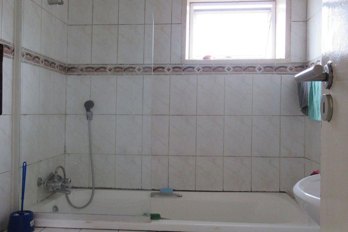 A dated bathroom featuring a bathtub with a glass shower screen, wall-mounted shower head, and tiled walls with a decorative border.
