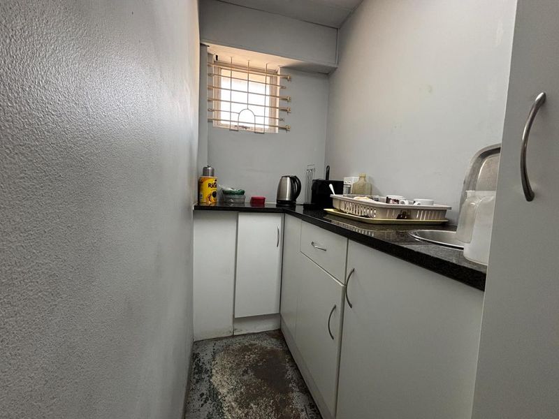 A compact scullery area featuring built-in white cabinetry, dark granite countertops, a stainless steel sink, and a security-grille window.