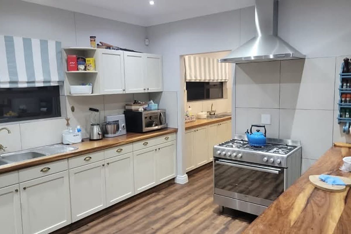 A well-maintained kitchen featuring light-toned cabinetry, wooden countertops, a stainless steel gas stove with extractor fan, and a secondary scullery area visible through the doorway.