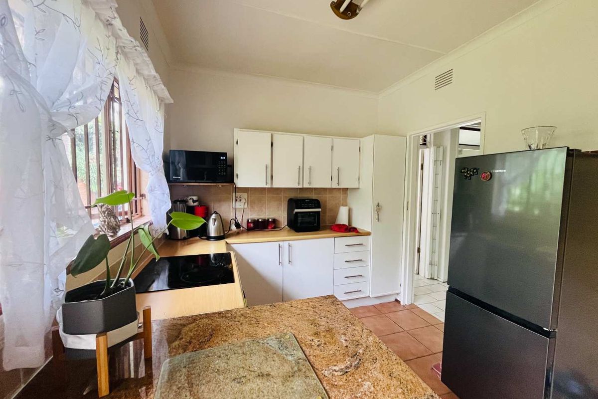 A functional kitchen featuring white cabinetry, granite countertops, a built-in electric hob, and tiled flooring, providing a practical workspace.