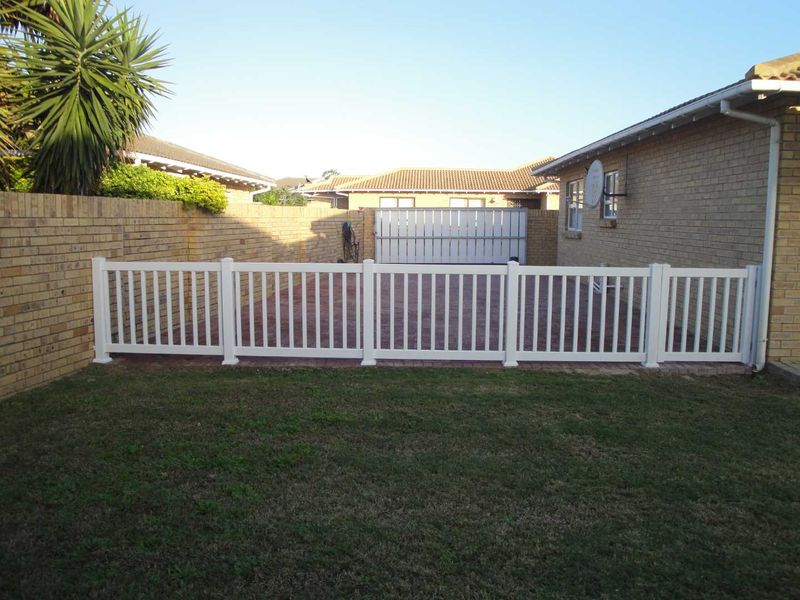 A private rear garden featuring a paved patio area, enclosed by a white picket fence and brick boundary walls.