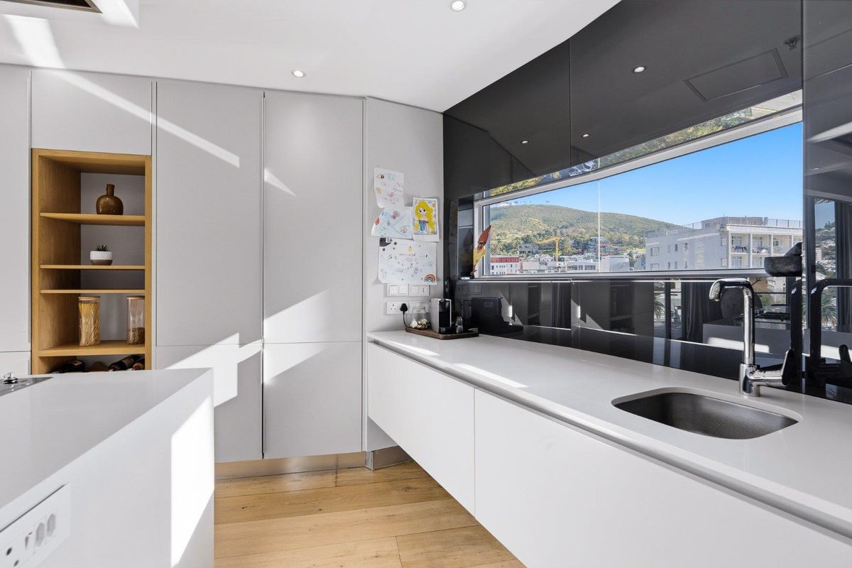 Modern kitchen featuring sleek handleless cabinetry, stone countertops, integrated sink, and timber flooring with a large window offering scenic mountain views.