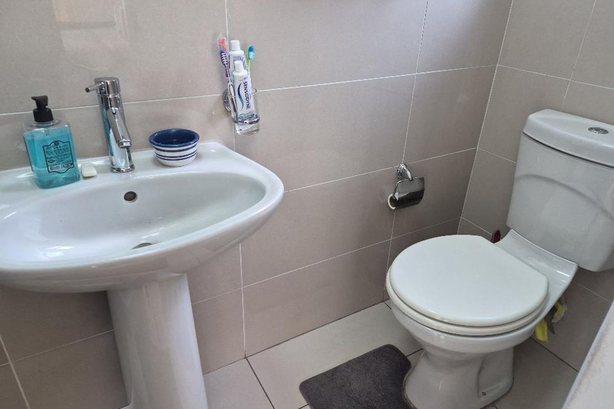 A clean and functional bathroom featuring a white pedestal basin, chrome mixer tap, and a standard white toilet with tiled walls and flooring.