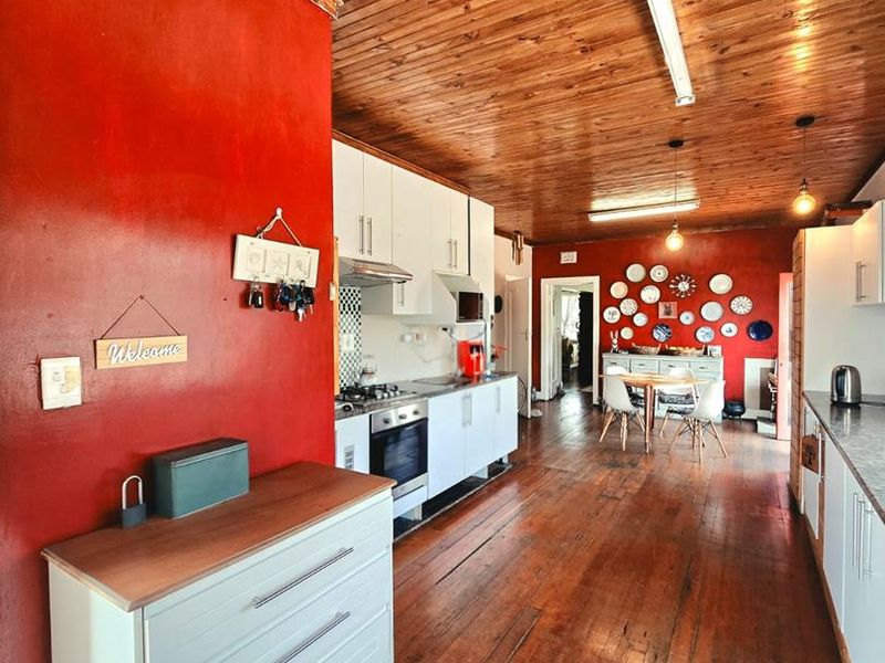 Open-plan kitchen and dining area featuring timber flooring, wood-paneled ceilings, and white cabinetry with integrated cooking appliances.
