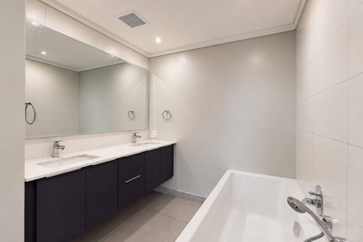 Modern bathroom featuring a sleek double vanity with undermount sinks, a large wall-to-wall mirror, and a clean built-in bathtub with chrome fixtures.