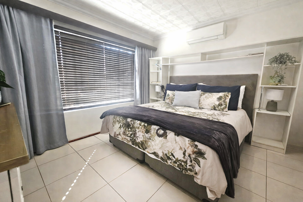 A well-lit bedroom featuring tiled flooring, a built-in headboard shelving unit, and a wall-mounted air conditioning unit.