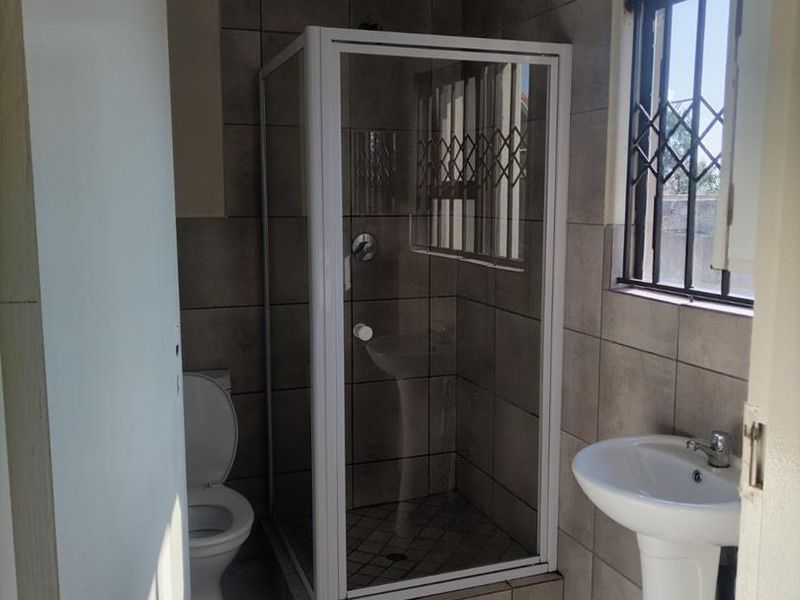 A functional bathroom featuring a shower enclosure, pedestal basin, and toilet, finished with neutral wall and floor tiling.