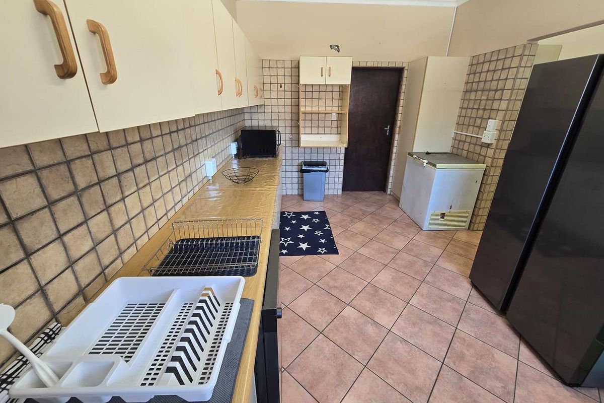 A functional kitchen featuring dated cabinetry, tiled splashbacks, and ceramic floor tiles, offering a practical layout with ample storage space.