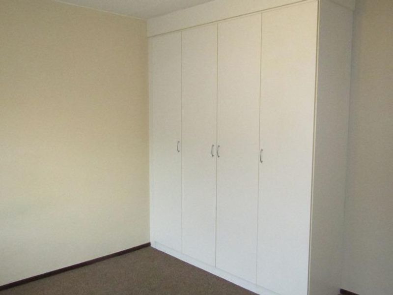 A clean, empty bedroom featuring neutral walls, carpeted flooring, and a large white built-in wardrobe providing ample storage space.