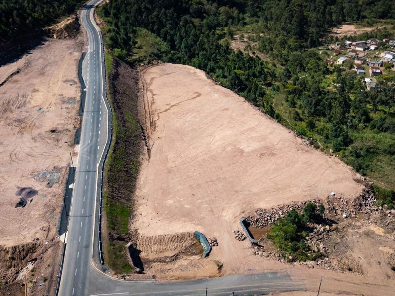 Aerial view of a large, cleared industrial development site adjacent to a paved road with established retaining infrastructure.