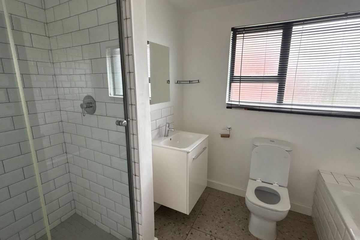 Modern bathroom featuring a glass-enclosed shower with subway tiling, a floating vanity, a toilet, and a bathtub with a window view.