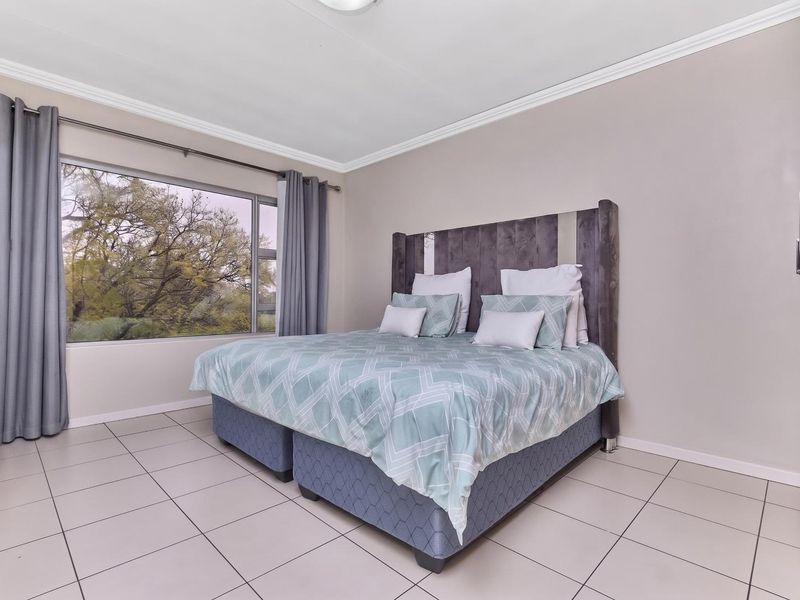 A well-lit bedroom featuring neutral tiled flooring, a large window with natural views, and built-in storage cabinetry.