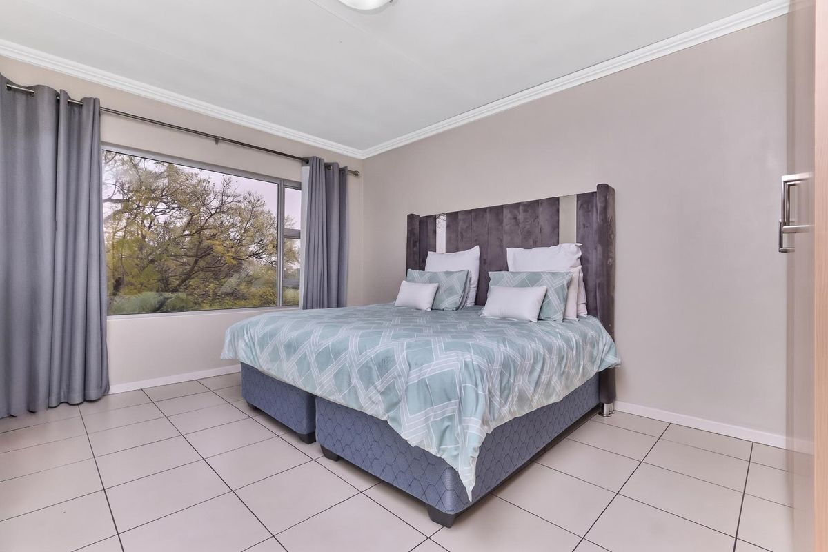 A well-lit bedroom featuring neutral tiled flooring, a large window with natural views, and built-in storage cabinetry.