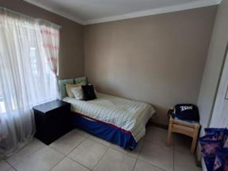 A compact bedroom featuring neutral wall tones, tiled flooring, and a built-in wardrobe, offering a functional and well-lit living space.
