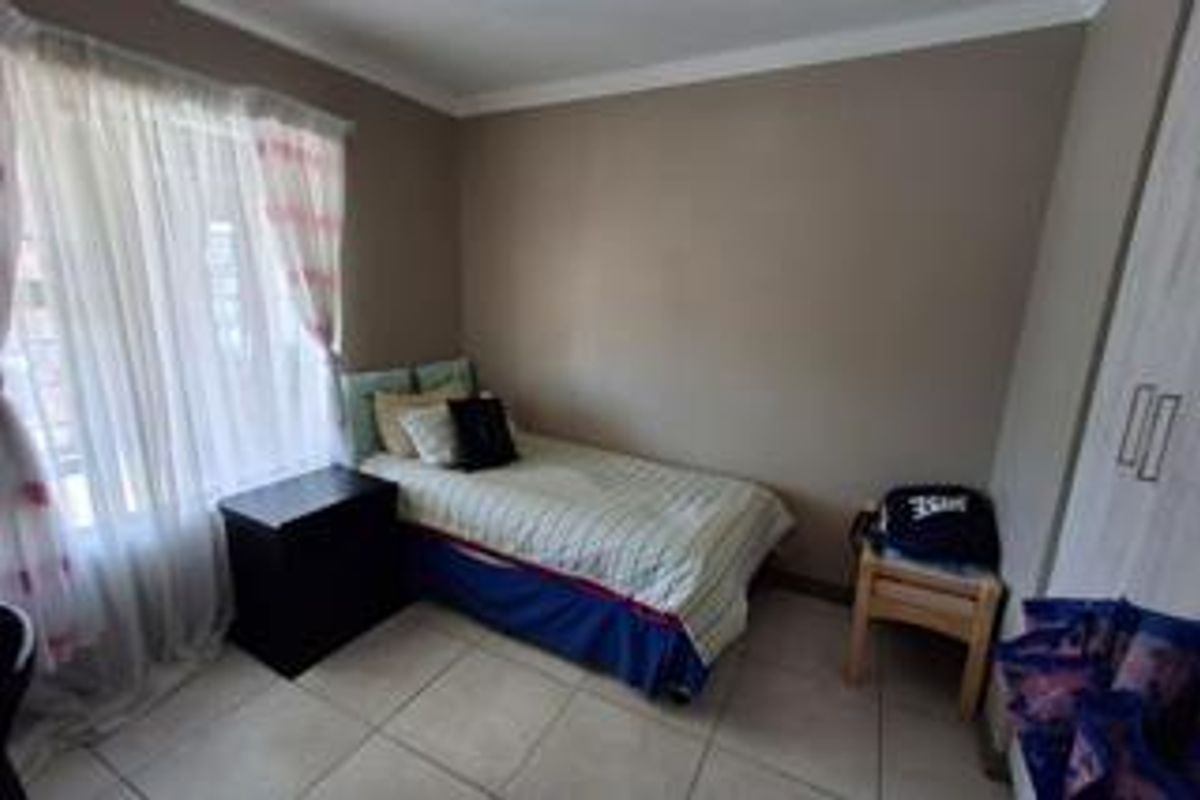 A compact bedroom featuring neutral wall tones, tiled flooring, and a built-in wardrobe, offering a functional and well-lit living space.