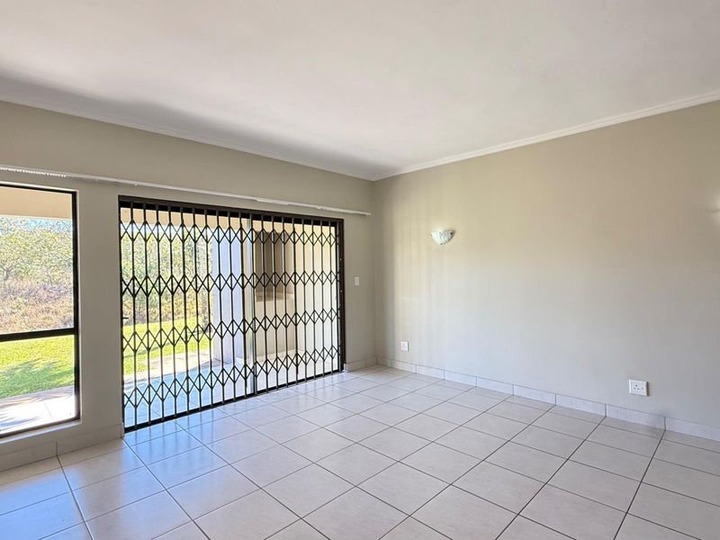 A bright, empty living area featuring neutral tiled floors, wall sconce lighting, and a sliding glass door with a security gate leading outdoors.